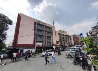 सडकबाट देखिएको वीर अस्पतालको आकस्मिक विभागको भवन र अगाडिका मानिस तथा सवारीसाधन।